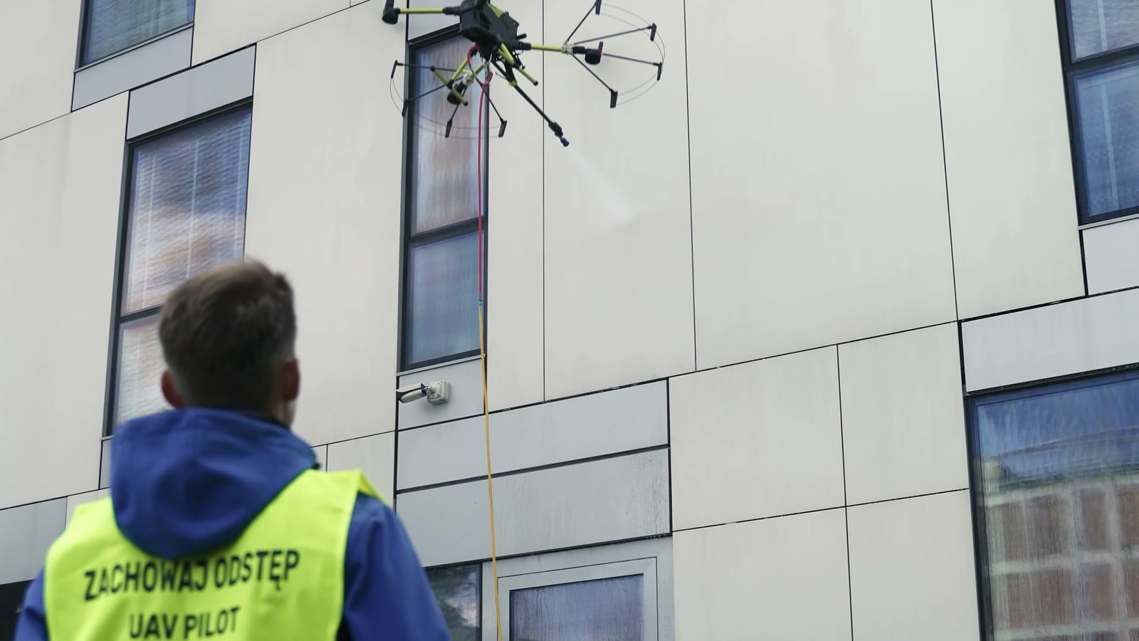Operator LUXMAR steruje dronem myjącym elewację z poziomu gruntu