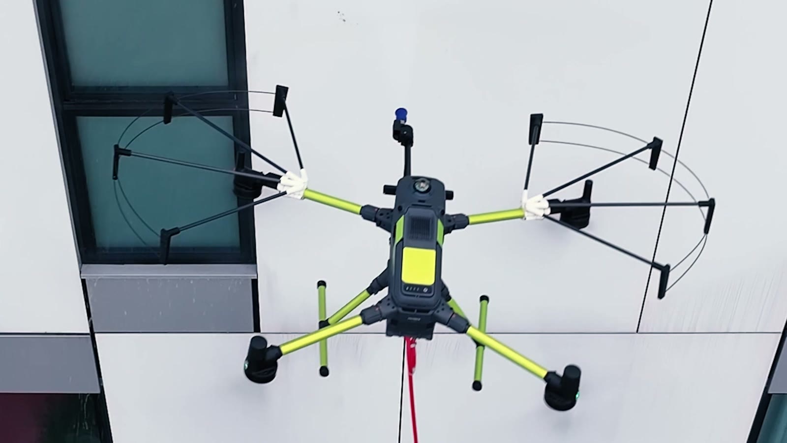 Dron z osłonami rotorów i lancą myjącą przy elewacji budynku